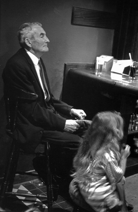 Limerick, Irlande &ndash; Septembre 1988 &laquo;&nbsp;Le gentleman et la petite fille&nbsp;&raquo;. Je crois me souvenir que cette image a &eacute;t&eacute; prise dans un pub qui sentait la cire encaustique, le bois et le tabac (on avait encore le droit de fumer &agrave; l'&eacute;poque...) de Limerick, sur la c&ocirc;te ouest irlandaise, dans un fond de baie comme l'&icirc;le en a le secret. Ce vieux monsieur tr&egrave;s digne semblait &ecirc;tre l&agrave; depuis toujours, il faisait partie du d&eacute;cor. J'aime bien le mouvement de la petite fille, un courant d'air dans cet univers feutr&eacute;. Merci &agrave; mon vieux Leica d'avoir &eacute;t&eacute; discret pour saisir cet instant.
