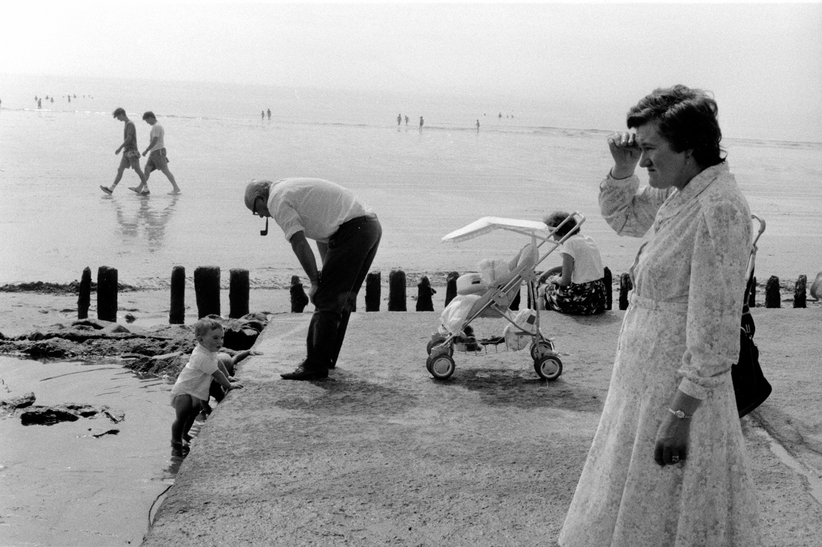 Rosslare, Irlande &ndash; Septembre 1988. En fait, je ne me souviens plus exactement de la date... 87, 88&nbsp;??? Peu importe. Cette image, prise au d&eacute;but d'un p&eacute;riple en Irlande, est typique de mon style photographique d'une &eacute;poque. Un m&eacute;lange de construction visuelle &agrave; la Henri Cartier-Bresson (en toute modestie, bien entendu &hellip;) que je v&eacute;n&eacute;rais, et d'humour &agrave; la Martin Parr ou &agrave; la Richard Kalvar (toujours en toute modestie!). Et puis, ce groupe d'Irlandais sur la plage de Rosslare, par un jour un peu gris, que faisaient-ils vraiment&nbsp;? Qu'est ce qu'elle regarde la dame, hein&nbsp;? Et le papy &agrave; la pipe, il ne pourrait pas l'enlever du sable vaseux, son petit-fils&nbsp;? Cette image, avec le temps, me para&icirc;t compl&egrave;tement d&eacute;cal&eacute;e, d'une autre &eacute;poque, les ann&eacute;es 50, Jacques Tati &hellip;