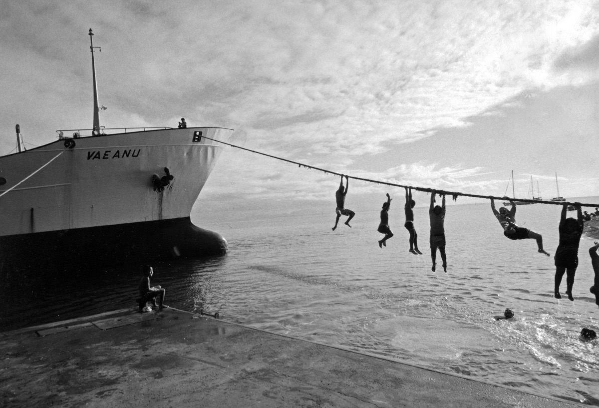Huahine, Iles sous le Vent, Polyn&eacute;sie - Mai 1993. Les enfants jouent sur le port, plongeant dans les eaux du lagon, suspendus aux amarres de la vieille &laquo;&nbsp;go&eacute;lette&nbsp;&raquo; qui fait la navette avec Tahiti, pour amener aux iliens les denr&eacute;es de premi&egrave;re &ndash; et aussi de seconde &ndash; n&eacute;cessit&eacute;. Nous avions voyag&eacute; toute la nuit dans la cabine pourrie d'un bateau comme celui-ci, entre les cafards et la rouille, hublots bris&eacute;s ouverts &agrave; tous les aliz&eacute;s et aux grains incessants. La mer &eacute;tait particuli&egrave;rement mauvaise, grande houle du Pacifique, et une otite contract&eacute;e en plongeant dans les patates de coraux contribuait largement &agrave; me donner le mal de mer. Il va sans dire que l'arriv&eacute;e &agrave; bon port &agrave; 4 heures du matin fut plut&ocirc;t bien accueillie. M&ecirc;me si la baraque qui tenant lieu de caf&eacute; sur les quais tardait &agrave; ouvrir...
