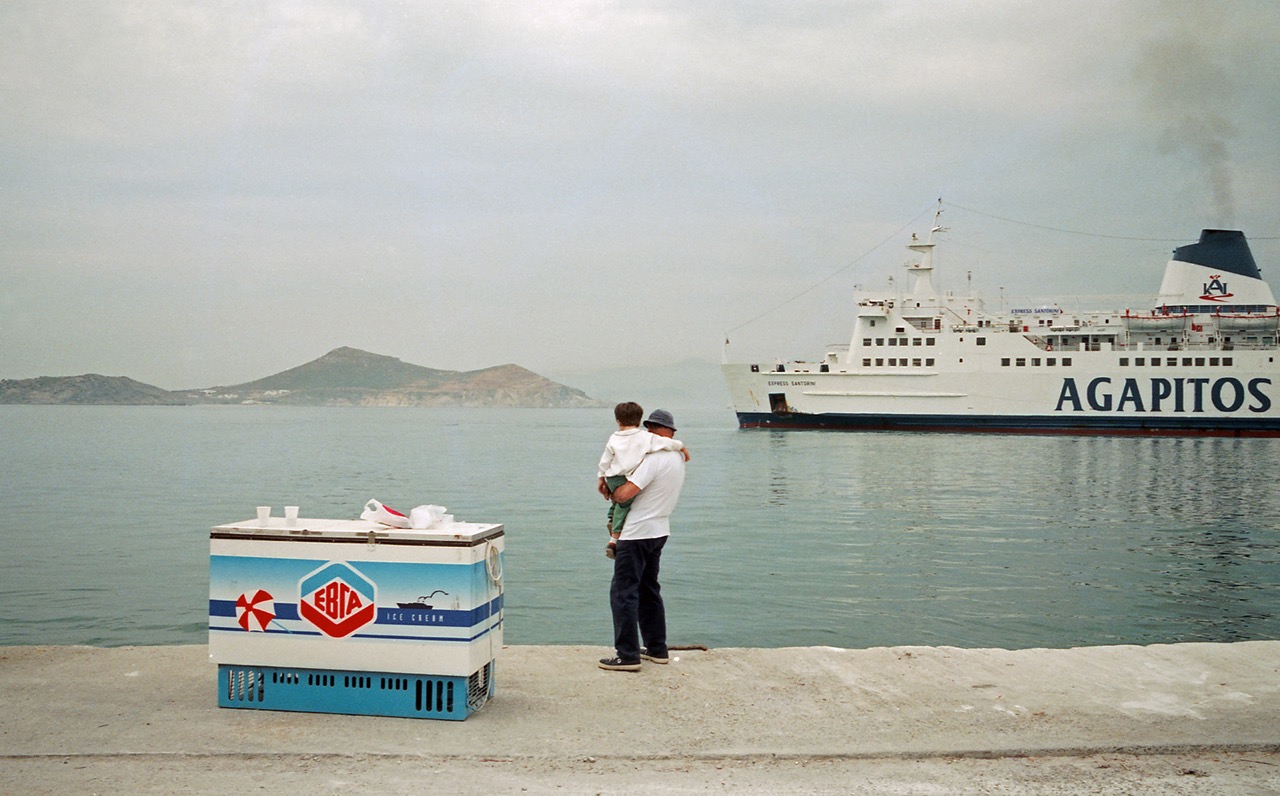 L'&nbsp;&raquo;Express Santorini&raquo; au port de Naxos &ndash; Gr&egrave;ce &ndash; juin 1997

&laquo;&nbsp;Au Pir&eacute;e, ce matin, justement, le ferry de 7 heures 30, c'est l'Apollon Express. Un jour sur deux, il fait la navette avec les &icirc;les. Le Santorini Express prend le relais. Ces bateaux n'ont d'&nbsp;&laquo;&nbsp;express&nbsp;&raquo; que le nom, ils accusent le poids des ans, s'arr&ecirc;tent partout, sont souvent en retard. Mais ils ont un charme fou. On y embarque dans un d&eacute;sordre bruyant, en c&ocirc;toyant le gitan pourvoyeur de poulets, le pope qui rejoint ses ouailles, le touristes en tongues et sac &agrave; dos, le vendeur ambulant de babioles qui quittera le bord juste avant l'appareillage. &laquo;&nbsp;&pi;&alpha;&rho;&alpha;&kappa;&alpha;&lambda;ώ, &pi;&alpha;&rho;&alpha;&kappa;&alpha;&lambda;ώ ...&nbsp;&raquo;, les consignes inaudibles gr&eacute;sillent. C'est parti pour 6 ou 7 heures de travers&eacute;e, ponctu&eacute;e par les aller-retours au bar, pour siroter un caf&eacute; frapp&eacute; ou grignoter un sandwich toast&eacute; insipide.&nbsp;&raquo;
Cette histoire et bien d'autres, vous pourrez les trouver sur mon nouveau site web &laquo;&nbsp;A la Porte d'Apollon, une chronique grecque 1980-2015&nbsp;&raquo;, en ligne ici&nbsp;: http://bit.ly/1RVxDxy. A propos, cette photo du c&eacute;l&egrave;bre vieux ferry est une de mes pr&eacute;f&eacute;r&eacute;es. Tout y est&nbsp;: le bateau bien s&ucirc;r, l'homme et son fils, le frigo &agrave; glaces... Qu'ajouter de plus&nbsp;?